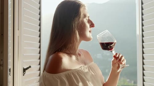 Woman relishing a glass of red wine on a villa terrace, while the picturesque mountains