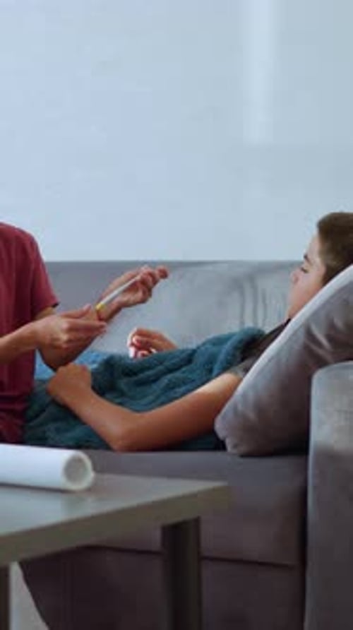 Mädchen überprüft das Thermometer, während der Bruder mit Taschentuch und Glas auf dem Tisch in der Nähe liegt