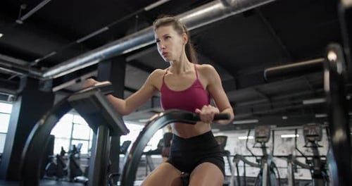 A Young Beautiful Woman in Sportswear is Training and Exercising on an Exercise Bike in a Gym