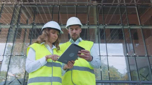 Man and Woman Engineers Have Conversation and using Tablet Computer on Construction Site. Glass Bui