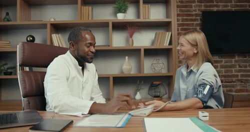 Black Doctor Measuring Blood Pressure to a Young Woman at Office