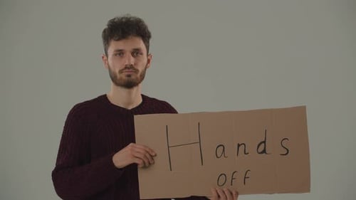 Un homme aux cheveux bouclés montre une pancarte « mains libres » à la caméra Un jeune manifestant qui proteste
