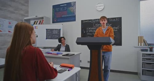 Focused Boy in Bright Orange Hoodie Delivers Class Presentation on Creative School Project