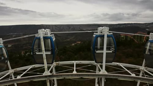 Closeup Aerial View of Ferris Wheel Spinning Around Against Mountains and Cloudy Sky