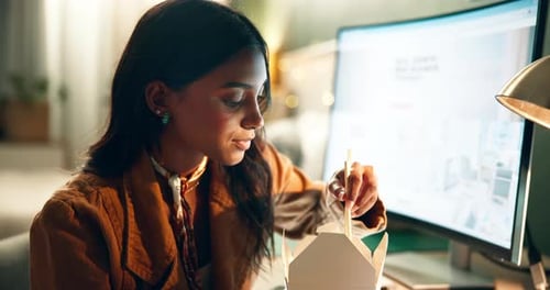 Young Woman Eating Noodles at Computer Desk
