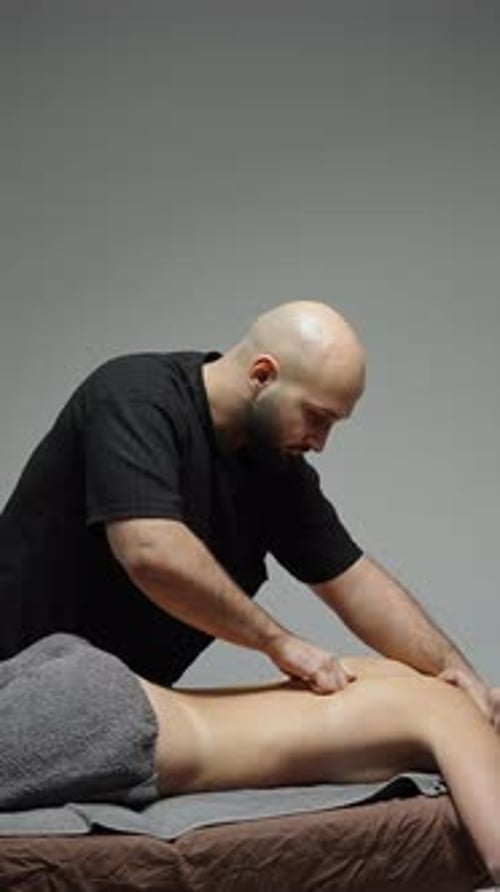 Professional Massage Therapist Performing Deep Tissue Back Massage on Client Lying on Table with