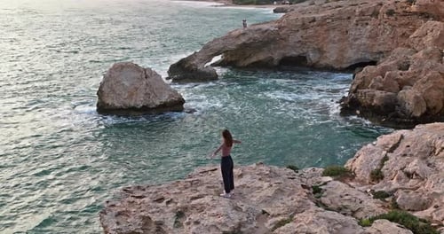 Aerial View of a Happy Woman on the Edge of the Rocks on the Seashore