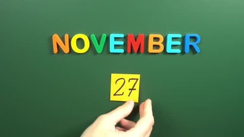 Hand sticking a sticker 27 November calendar day on school board. 27 date of November. Twenty