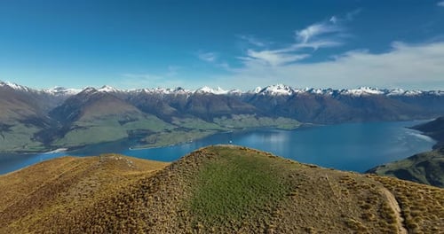 Man standing next to wooden summit pole on Isthmus Peak with Southern Alps view