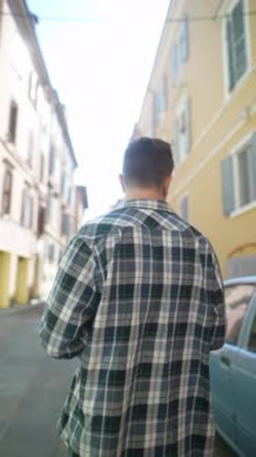 A Young Man Strolls Through a European City in a Plaid Shirt Radiating a Casual Urban Vibe