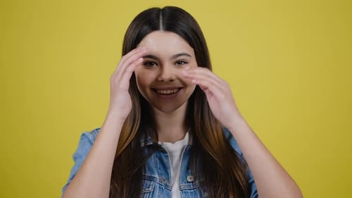 Smiling Teen Girl Touches Her Hair on Yellow Background