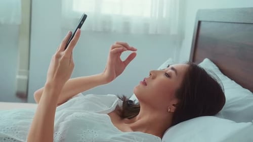 Woman Lying in Bed Using Her Smartphone