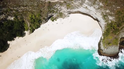 Bird's Eye drone shot above tourists relaxing on KelingKing beach while large waves crash onto the s