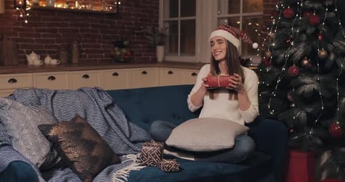 Woman Opening Christmas Present on Couch by Tree