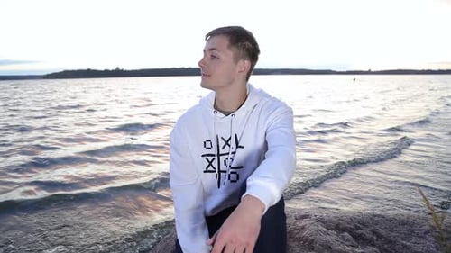 Young teenager relaxing while siting on the rod near the lake shore in the evening
