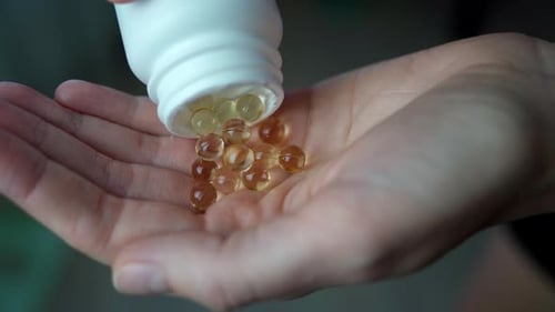 Close-up of a woman pouring vitamin D or omega-3 into her hand.