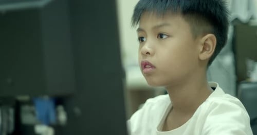 An Asian boy in elementary school is having fun using his desktop computer to play games