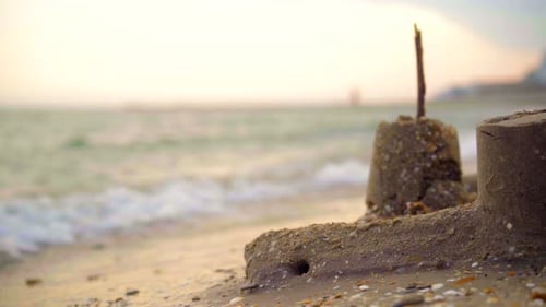 Sea waves crashing on a sand castle at sunset on a sand beach