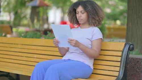 Woman Reads Document on Park Bench Reacts Positively