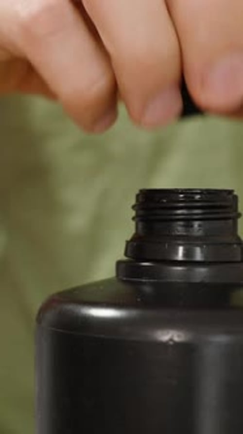 Vertical video. Black Bottle with Some Red Drink, Man Pouring It into a Measuring Cup and Drinking