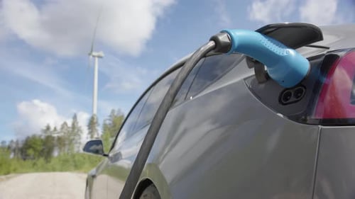 WIDE SHOT - A generic electric car charges in front of a wind turbine