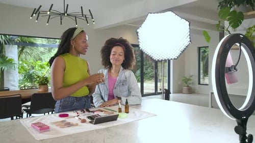 Instructora femenina que sostiene una base compacta para mezclar y espolvorear en la cara de la modelo con un cepillo en la cocina