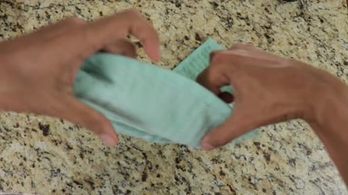Hands using and folding green towel, top down view