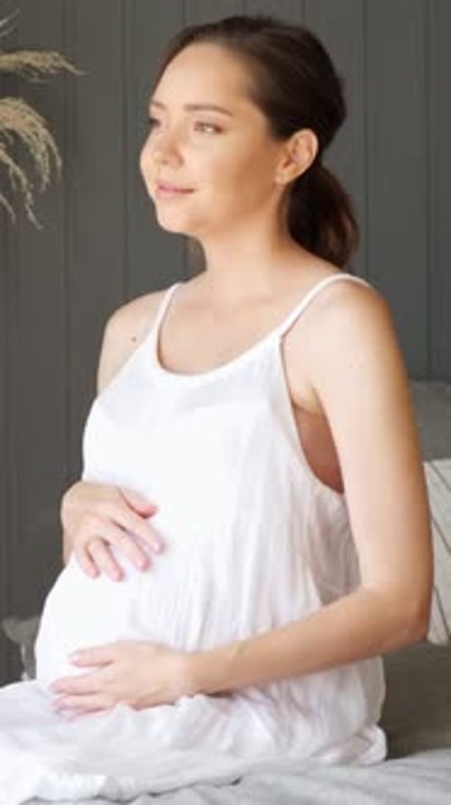 Pregnant Caucasian Woman Sitting On Bed Practicing Prenatal Yoga Breathing And Gentle Belly Massage