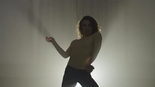 Silhouette einer Frau, die in einem weißen Lichtstrahl einen Ausdruckstanz aufführt