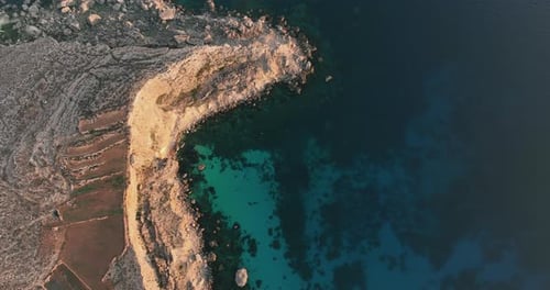 Sunset drone footage capturing the seaside cliffs and crystal clear water on the coastline of Malta.