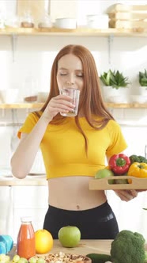 Woman Holding Vegetables and Drinking Water in Kitchen