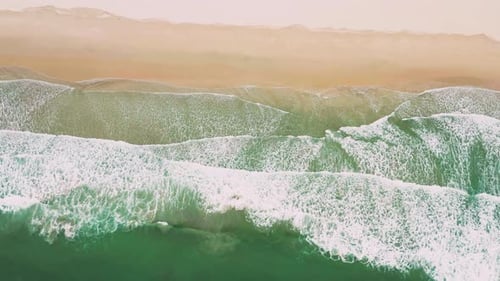 Aerial views of flying over stunning sandy beach with tropical waves rolling into the shore.
