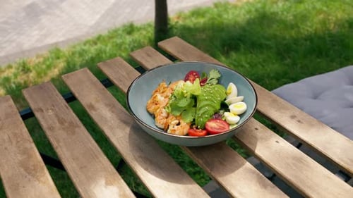 Close Up in a Restaurant on the Street on Plank Table a Blue Plate with a Warm Salad with Avocado