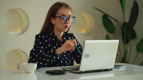 Happy Young Woman Using a Laptop Sitting at a Desk Writing Notes While Watching a Webinar Studying