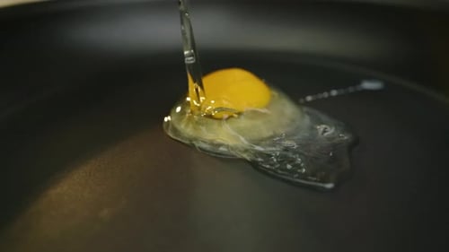 Bright yellow egg yolk falling into hot pan to make fried egg in slow motion