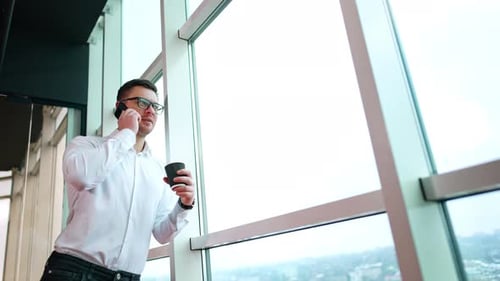 Relaxed smiling Caucasian male leaning on the window in office.