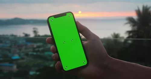 Close Up Male Holding Phone with Green Screen Chroma Key Over Sunset at Sea at Tropical Scenery Male