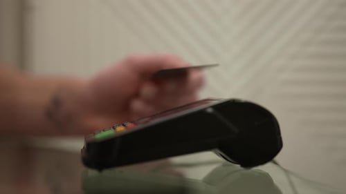 Vista lateral de primer plano de un cliente varón irreconocible que paga con una tarjeta de crédito sin contacto con NFC