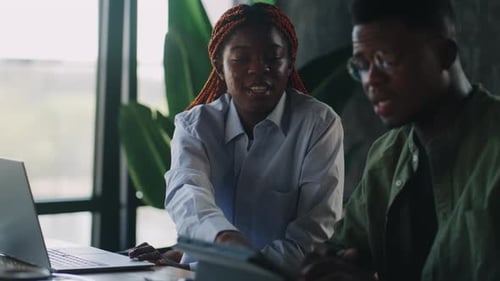 At a Cafe Sitting Near a Laptop and Gesturing with Their Hands and Pointing at the Screen are Two