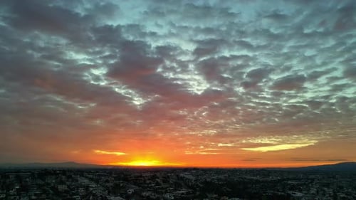 The sun rises just above the horizon in a cloud-covered sky over a city.