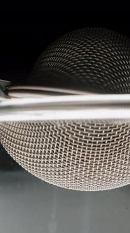 Vertical video. Placing a metal sieve with tea leaves into the glass of water, and tiny particles