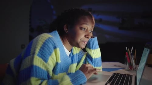 Young Black American Female Student Bored and Tired Writing and Using Laptop Sitting at Desk Home