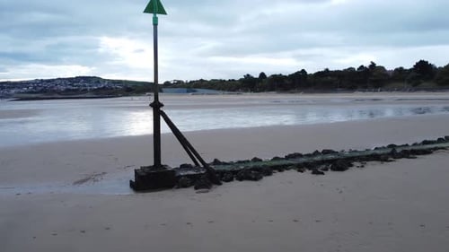 Coastal tide marker aerial view low slow push in left across moody overcast low tide seaside beach