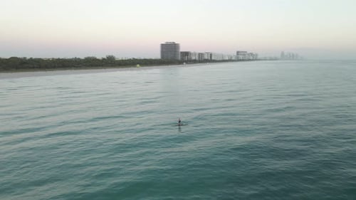 Orbiting aerial of stand up ocean paddleboarder alone off Miami Beach