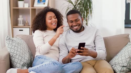 Smiling Couple Relaxing Together Looking at Smartphone Indoors
