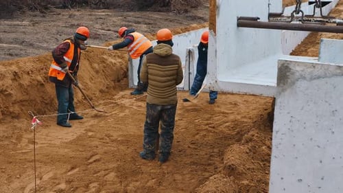 Bau eines Hauses: Arbeiter räumen einen Platz mit Schaufeln für das Fundament von Betonplatten
