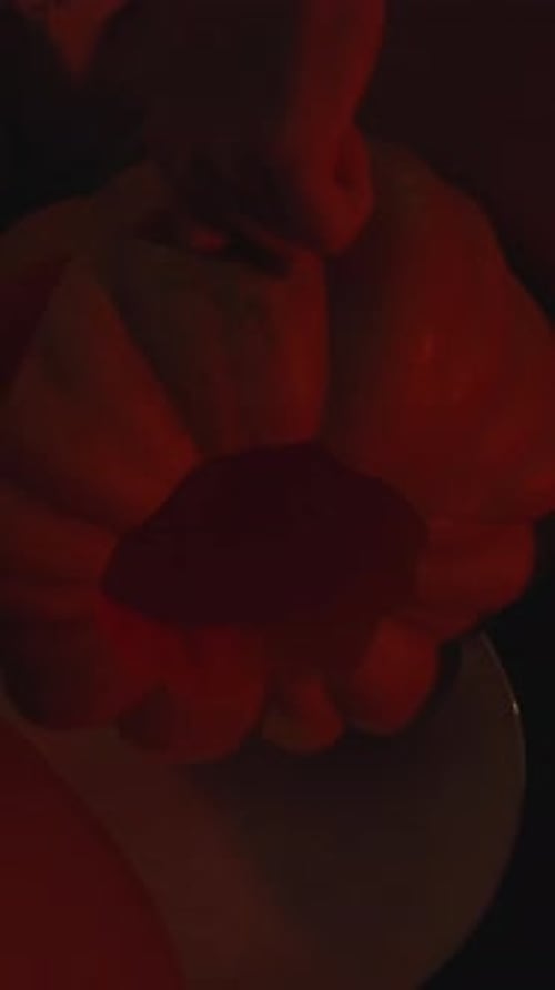Vertical video. A young woman in the darkness, illuminated by candlelight, carves out the eyes of a
