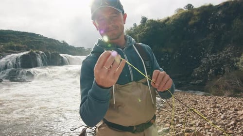 Man Prepares Fishing Line by Mountain River