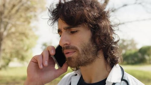 Long Hair Male Doctor Talks On The Phone Bad News Outside The Hospital