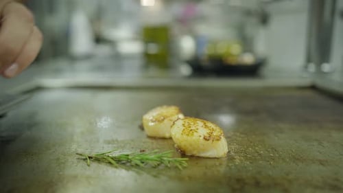 Plan au ralenti de pétoncles ramassés sur une plaque chauffante à l'aide d'une spatule dans une cuisine raffinée